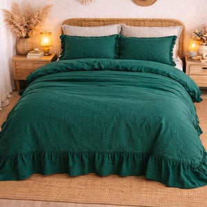 May include: A bed dressed with a dark green duvet cover and matching pillowcases. The duvet features a ruffled trim. The bed has a woven headboard, and the room has a neutral colour scheme with decorative elements.