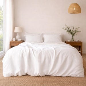 Könnte beinhalten: Ein Schlafzimmer mit einem Bett mit weißer Bettwäsche und Kissen, das auf einem gewebten Teppich steht. Zwei Nachttische aus Holz mit Lampen und Ornamenten befinden sich auf beiden Seiten des Bettes. Eine gewebte Pendelleuchte hängt darüber, und ein Fenster mit transparenten Vorhängen ist sichtbar.