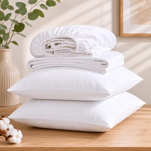 May include: A stack of white bedding consisting of two rectangular pillows at the bottom, a folded flat sheet in the middle, and a fitted sheet with elastic edges on top. The fabric has a visible woven texture and a clean, bright white finish.
