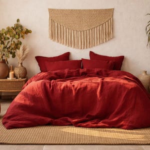 Peut inclure: Une chambre à coucher avec un lit recouvert d'une housse de couette en lin rouge foncé et d'oreillers assortis. Une tenture murale tissée et une grande plante en pot ajoutent à l'esthétique bohème de la pièce. Un tapis tissé et un pouf rond complètent le décor.