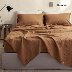 May include: A bed set in a cinnamon brown colour featuring two rectangular pillows and a flat sheet draped over a mattress. The bedding has a visible textured fabric finish. The word Cinnamon is printed in the upper right corner of the image.