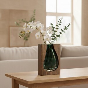 Op de afbeelding: Een moderne houten vaas met een donkergroene glazen inzet, met witte orchideeën en groene eucalyptus takken. De vaas staat op een lichtgekleurde houten tafel, wat een minimalistische uitstraling creëert.
