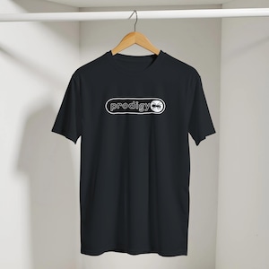 May include: A black short-sleeved t-shirt featuring a white graphic on the chest. The graphic consists of a horizontal pill-shaped outline containing the lowercase text "prodigy" followed by a circular icon depicting a black ant silhouette.