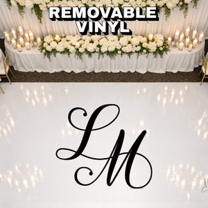 May include: A white dance floor with a large black monogram of the letters "LM". The floor is surrounded by tables with white tablecloths, floral arrangements, and candles. The text "REMOVABLE VINYL" is at the top.