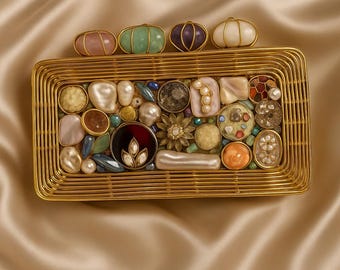 Puede incluir: Un clutch rectangular dorado con un diseño de estructura de alambre. El clutch está adornado con una variedad de piedras decorativas coloridas, perlas y detalles florales. La parte superior presenta una fila de piedras ovaladas de varios colores. El texto "VELVET PEARL STUDIO" está en la parte inferior.