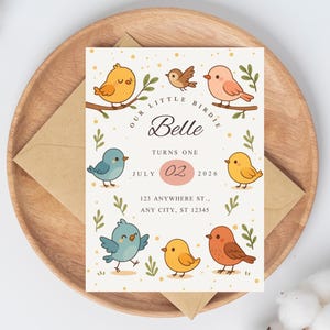 May include: A birthday invitation featuring cartoon birds in various colors, including yellow, blue, and orange, with the text "Our Little Birdie Belle Turns One" and event details. The invitation is on a cream background, placed on a wooden plate with a brown envelope.