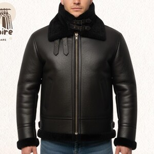 Puede incluir: Chaqueta de cuero negro con cuello y puños de borrego. La chaqueta tiene cremallera frontal y detalles de hebilla. El logotipo "Empire Outwears" es visible en la esquina superior izquierda.