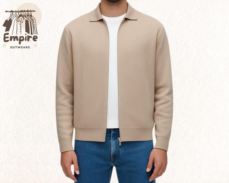 Pode incluir: Casaco bege com z&iacute;per e gola, usado sobre uma camiseta branca e jeans azuis. O casaco tem z&iacute;per completo e punhos canelados. O logotipo "Empire Outwears" &eacute; vis&iacute;vel no canto superior esquerdo.