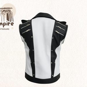 Pode incluir: Um colete sem mangas preto e branco com z&iacute;peres e tachas prateadas. O colete tem gola e acabamentos pretos, com um painel central branco. O logotipo da marca "Empire Outwears" est&aacute; no canto superior esquerdo. Uma pe&ccedil;a de vestu&aacute;rio elegante.