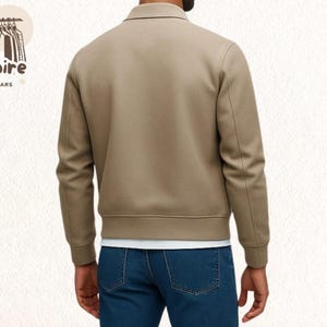 Pode incluir: Casaco bege com gola e mangas compridas. O casaco tem bainha e punhos canelados. A pessoa est&aacute; usando jeans azuis e uma camiseta branca por baixo. O logotipo "Empire Outwears" &eacute; vis&iacute;vel no canto superior esquerdo.