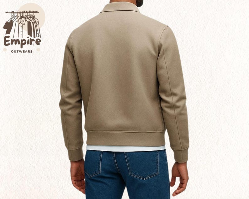Pode incluir: Casaco bege com gola e mangas compridas. O casaco tem bainha e punhos canelados. A pessoa est&aacute; usando jeans azuis e uma camiseta branca por baixo. O logotipo "Empire Outwears" &eacute; vis&iacute;vel no canto superior esquerdo.