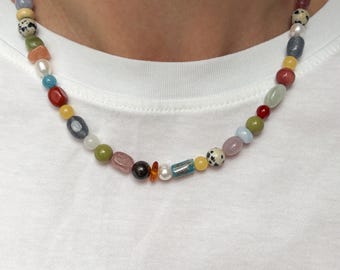 Peut inclure: Un collier de perles composé d'une variété de pierres multicolores, incluant des perles rondes lisses, des gemmes de formes irrégulières, des perles blanches et des perles de jaspe dalmatien à taches noires, disposées en un seul rang.