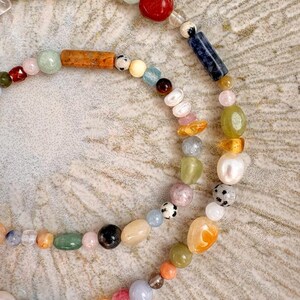 May include: A close-up of two beaded necklaces. The necklaces feature a variety of colorful gemstones and beads, including red, blue, green, and orange. The beads are strung together on a delicate string, creating a unique and eye-catching design.