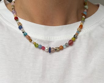 Peut inclure: Un collier de perles composé d'une variété de petites pierres multicolores, de perles et de perles en verre dans des tons de bleu, rouge, jaune, vert et blanc. Les perles sont disposées sur un seul rang avec des formes et textures variées.