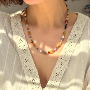 May include: A colorful beaded necklace with a variety of shapes and sizes of beads. The beads are in shades of pink, orange, yellow, green, blue, and brown. The necklace is worn around the neck.