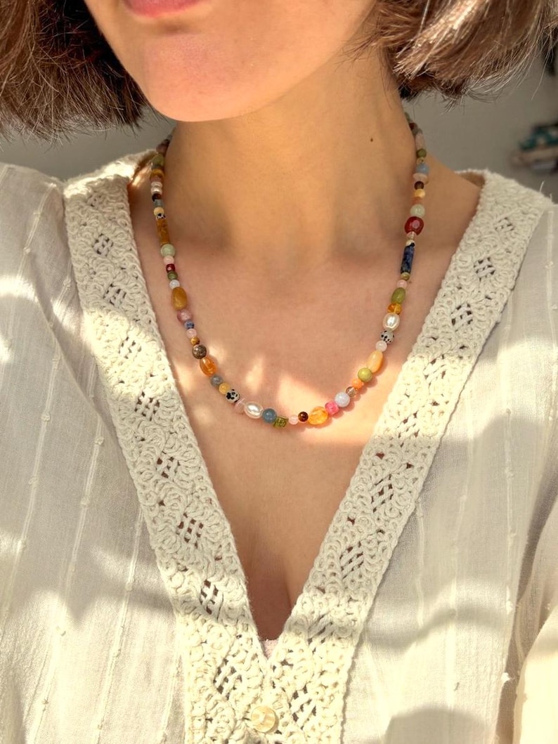 May include: A colorful beaded necklace with a variety of shapes and sizes of beads. The beads are in shades of pink, orange, yellow, green, blue, and brown. The necklace is worn around the neck.