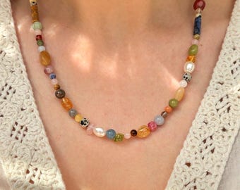 Peut inclure: Un collier de perles multicolores avec une variété de perles de pierres précieuses dans les tons de rose, jaune, vert et bleu. Le collier comprend un mélange de perles rondes, ovales et de forme irrégulière, enfilées sur une chaîne délicate.