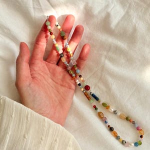 May include: A colorful beaded necklace with a variety of shapes and sizes of beads. The beads are in shades of red, yellow, green, blue, and brown. The necklace is held against a white background.