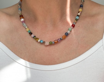 Peut inclure: Un collier de perles composé d'une variété de petites pierres et perles multicolores dans des tons de bleu, vert, jaune, rouge, orange et blanc. Le collier est formé de perles rondes, ovales et de formes irrégulières enfilées sur un seul rang.