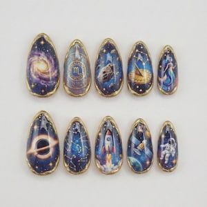 May include: A set of ten almond-shaped artificial nails with a gold trim. Each nail features a different space-themed design, including galaxies, constellations, rockets, and astronauts, set against a dark blue background.