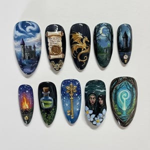 May include: A set of ten almond-shaped, painted nail art designs. Each nail features a different fantasy-themed image, including a castle, a dragon, a scroll, a bonfire, a key, and a potion bottle. The color palette includes blues, greens, and golds.
