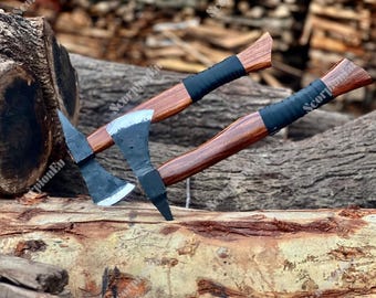 Peut inclure: Deux haches avec des manches en bois et des lames noires sont présentées. Les manches sont d'un brun riche, enveloppés d'un matériau noir près de la tête. Les haches reposent sur une surface en bois, mettant en valeur leur savoir-faire.