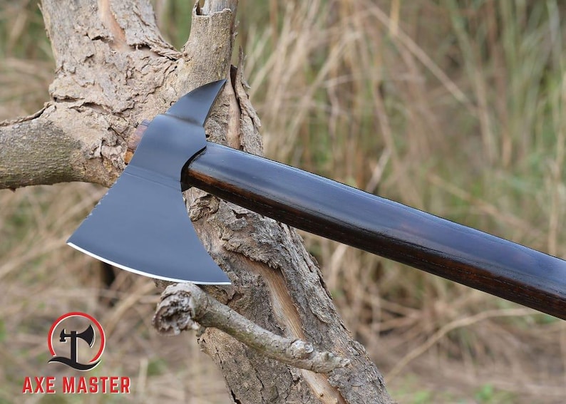 Pode incluir: Machado com cabe&ccedil;a preta e cabo de madeira escura. A cabe&ccedil;a do machado tem uma l&acirc;mina curva e uma ponta no lado oposto. O cabo &eacute; liso e polido. O logotipo Axe Master est&aacute; no canto inferior esquerdo.