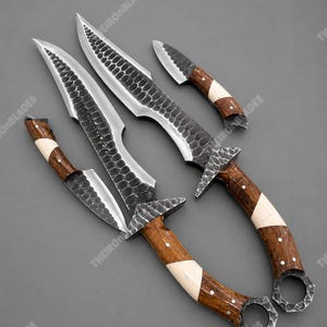 Könnte beinhalten: Ein Set aus vier Messern mit dunklen, gehämmerten Metallklingen, die eine schuppenartige Textur aufweisen. Die Griffe bestehen aus abwechselnden Segmenten aus dunklem Holz und hellem Material, befestigt mit kleinen Metallstiften und Ringknäufen.