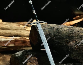 Puede incluir: Una espada de estilo medieval con una hoja plateada y una guarda ornamental. El mango es negro con detalles plateados. La espada se exhibe sobre un fondo de troncos de madera.
