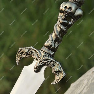 May include: A decorative sword with a silver blade and an ornate handle. The handle features a skull design with a crown and a serpent wrapped around it. The sword's hilt has an intricate, detailed design.