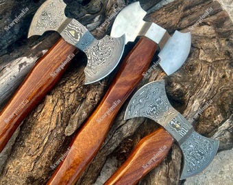Könnte beinhalten: Vier Äxte mit gemusterten Stahlklingen und Holzgriffen. Die Klingen haben ein einzigartiges Design und die Griffe sind in einem satten, dunklen Braun gehalten. Die Äxte sind auf einer strukturierten Holzoberfläche angeordnet.