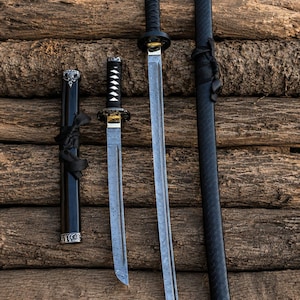 Może przedstawiać: Katana i krótszy miecz tanto, oba z ostrzami ze stali wzorzystej, czarnymi owiniętymi rękojeściami i okrągłymi gardami. Każdemu mieczowi towarzyszy pasująca czarna pochwa z czarnym sznurkiem i srebrnymi akcentami z metalu.