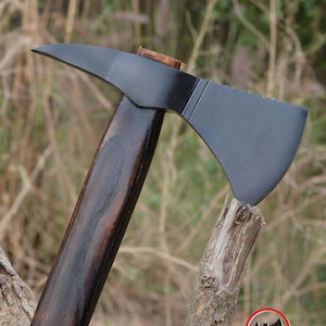 Pode incluir: Machado com l&acirc;mina preta e cabo de madeira escura. A cabe&ccedil;a do machado &eacute; cinza escuro. O cabo &eacute; marrom escuro. O machado est&aacute; apoiado em um peda&ccedil;o de madeira. O logotipo Axe Master est&aacute; no canto inferior direito.