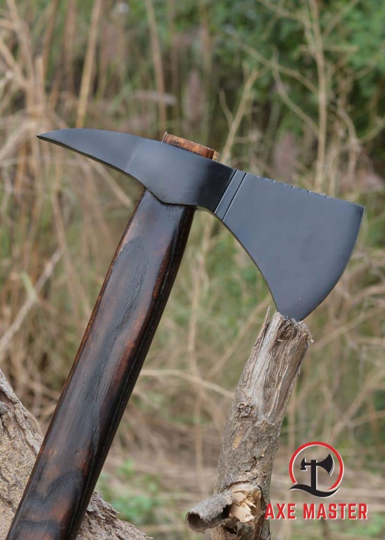 Pode incluir: Machado com l&acirc;mina preta e cabo de madeira escura. A cabe&ccedil;a do machado &eacute; cinza escuro. O cabo &eacute; marrom escuro. O machado est&aacute; apoiado em um peda&ccedil;o de madeira. O logotipo Axe Master est&aacute; no canto inferior direito.