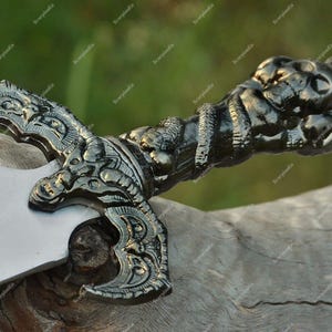 May include: A detailed, ornate dagger with a silver blade and a dark, intricately designed handle. The handle features sculpted figures and a textured grip, suggesting a historical or fantasy theme.