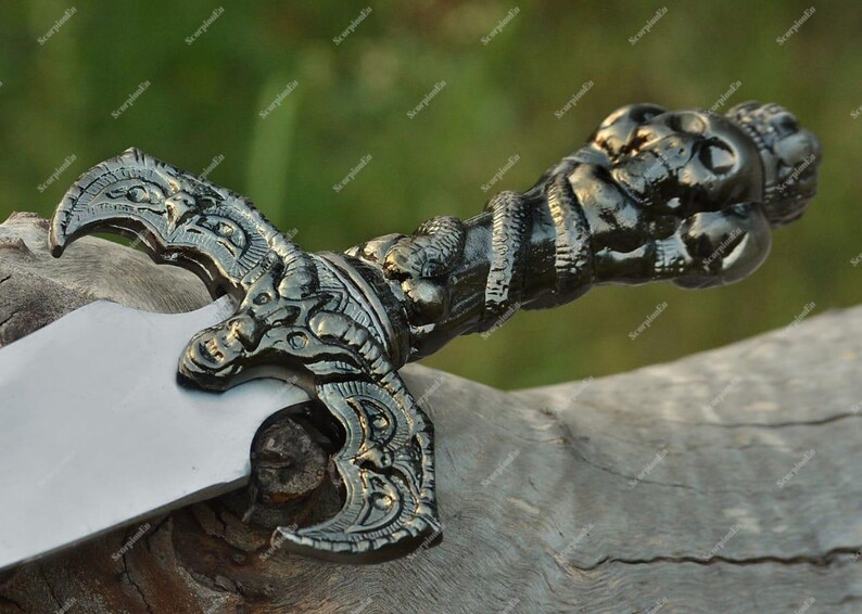 May include: A detailed, ornate dagger with a silver blade and a dark, intricately designed handle. The handle features sculpted figures and a textured grip, suggesting a historical or fantasy theme.