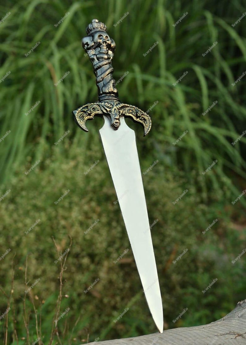 May include: A decorative dagger with a silver blade and an ornate handle. The handle features a skull design at the top and a twisted, serpent-like pattern. The hilt has an intricate, gold-colored design.