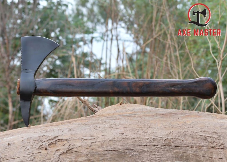 Pode incluir: Machado com cabo de madeira escura e cabe&ccedil;a preta. A cabe&ccedil;a do machado tem uma l&acirc;mina afiada e uma ponta no lado oposto. O cabo &eacute; curvo para a ader&ecirc;ncia. O machado est&aacute; apoiado em um tronco.