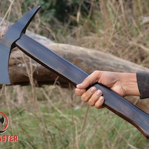 Pode incluir: Machado com uma l&acirc;mina cinza escuro e um cabo de madeira escura. A cabe&ccedil;a do machado tem um topo curvo e uma borda dentada. A al&ccedil;a &eacute; segurada em uma m&atilde;o. O logotipo Axe Master est&aacute; no canto inferior esquerdo.