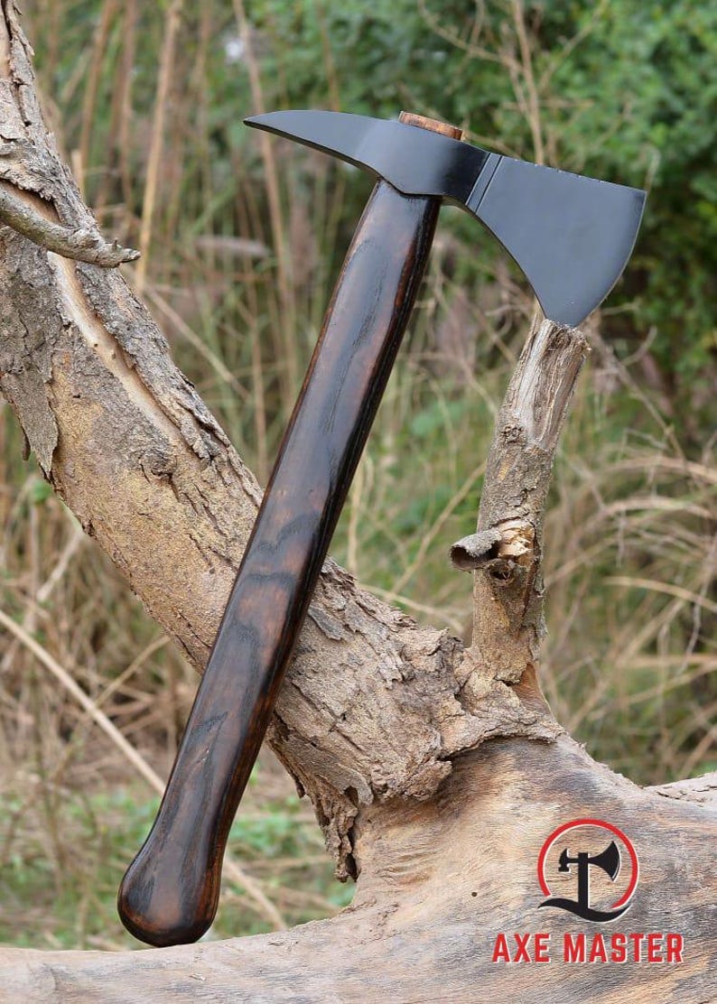 Pode incluir: Machado com cabo de madeira escura e polida e l&acirc;mina preta. O machado est&aacute; apoiado em um galho de &aacute;rvore desgastado, com o logotipo Axe Master vis&iacute;vel no canto inferior direito. O cabo tem uma extremidade curva para uma pegada segura.