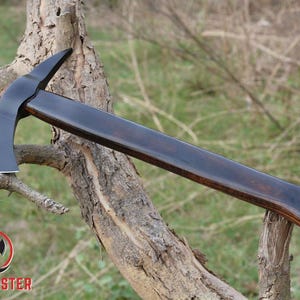 Pode incluir: Machado com cabo de madeira escura e polida e cabe&ccedil;a de machado preta. O machado est&aacute; apoiado num galho de &aacute;rvore. O log&oacute;tipo "AXE MASTER" &eacute; vis&iacute;vel no canto inferior esquerdo.