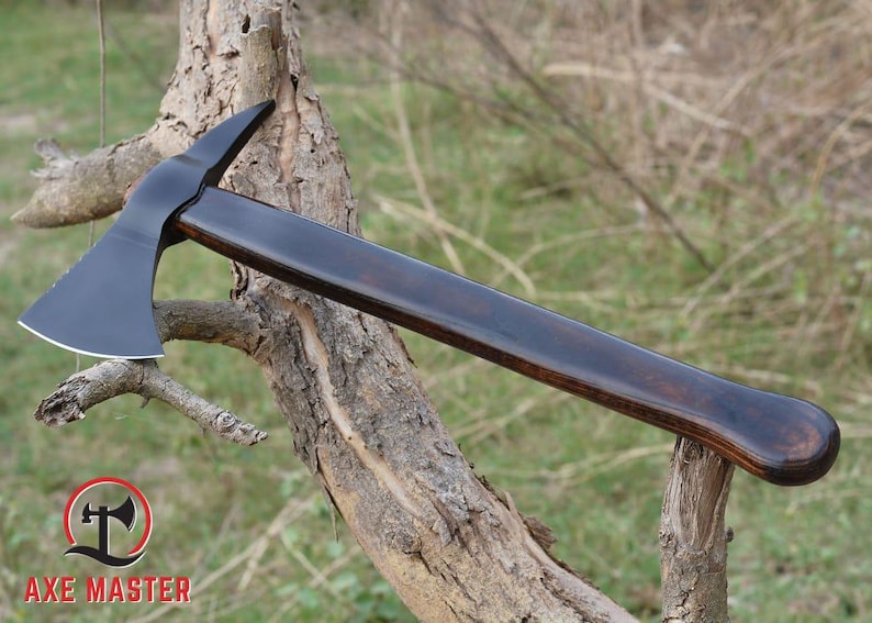 Pode incluir: Machado com cabo de madeira escura e polida e cabe&ccedil;a de machado preta. O machado est&aacute; apoiado num galho de &aacute;rvore. O log&oacute;tipo "AXE MASTER" &eacute; vis&iacute;vel no canto inferior esquerdo.