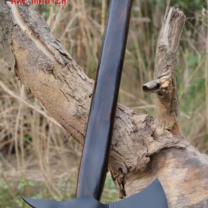 Pode incluir: Machado com cabo de madeira escura e cabe&ccedil;a preta. A cabe&ccedil;a do machado tem uma l&acirc;mina afiada e uma borda serrilhada. O cabo &eacute; longo e curvo, com o texto "AXE MASTER" em vermelho.