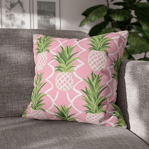 May include: Square decorative pillow with a pink background featuring a repeating pattern of green and white pineapples. The pineapples have a white lattice design and are set against a white geometric trellis.