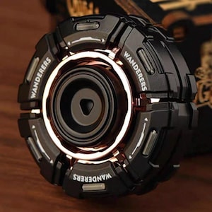 May include: Black and gold-toned fidget spinner with the word "Wanderers" printed on the outer rim. The center has a circular design with a gold-colored ring. The spinner has a futuristic, mechanical aesthetic.