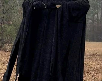 May include: A person in a black hooded robe and a white Scream mask stands outdoors. The costume has long sleeves and a fringed hem. The background features a field and trees, creating a spooky atmosphere.