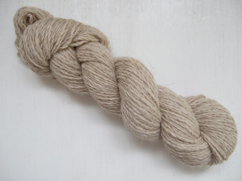 May include: A skein of natural-colored yarn, tightly twisted into a rope-like form. The yarn is a light beige color, with visible fibers and a slightly textured appearance. The yarn is likely made of natural fibers, suitable for knitting or crocheting projects.
