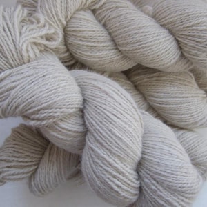 May include: Close-up of several skeins of undyed, light beige yarn. The yarn is thick and appears to be made of natural fibres. The skeins are loosely arranged, showing the texture and volume of the yarn. Ideal for knitting and crochet projects.