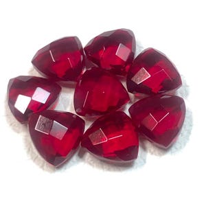 Può includere: Una collezione di otto gemme a forma di cuore, sfaccettate, rosso intenso. Ogni gemma ha molteplici sfaccettature che catturano la luce, creando un effetto scintillante. Le gemme sono disposte vicine, mostrando il loro colore e la loro forma vivaci.