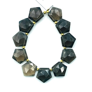 Peut inclure: Un collier de perles de pierres précieuses en quartz fumé facetté. Chaque perle est d'une couleur gris-brun foncé et translucide, avec une forme géométrique pentagonale. Les perles sont enfilées avec des accents métalliques dorés.